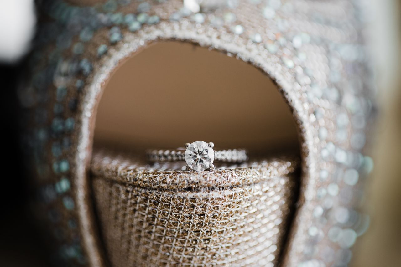 A side stone engagement ring sits in the toe of a sparkly nude heel.