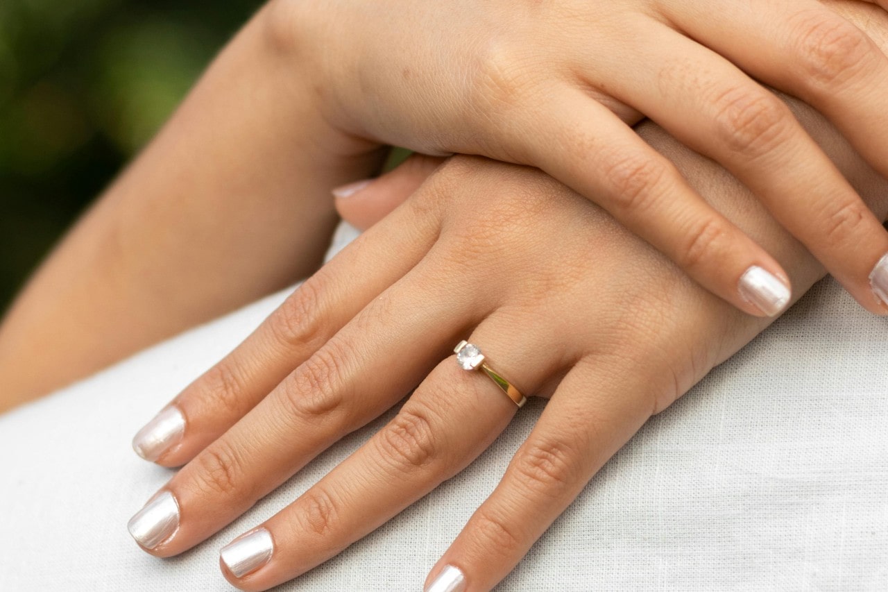 a woman’s hands, one place on top of the other, wearing a solitaire engagement ring