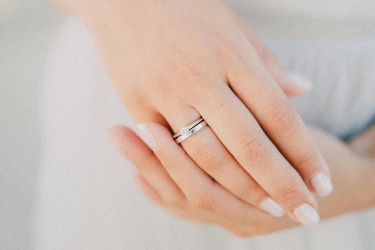A close-up of a woman’s hands, with emphasis on her engagement ring stacked atop a simple band.