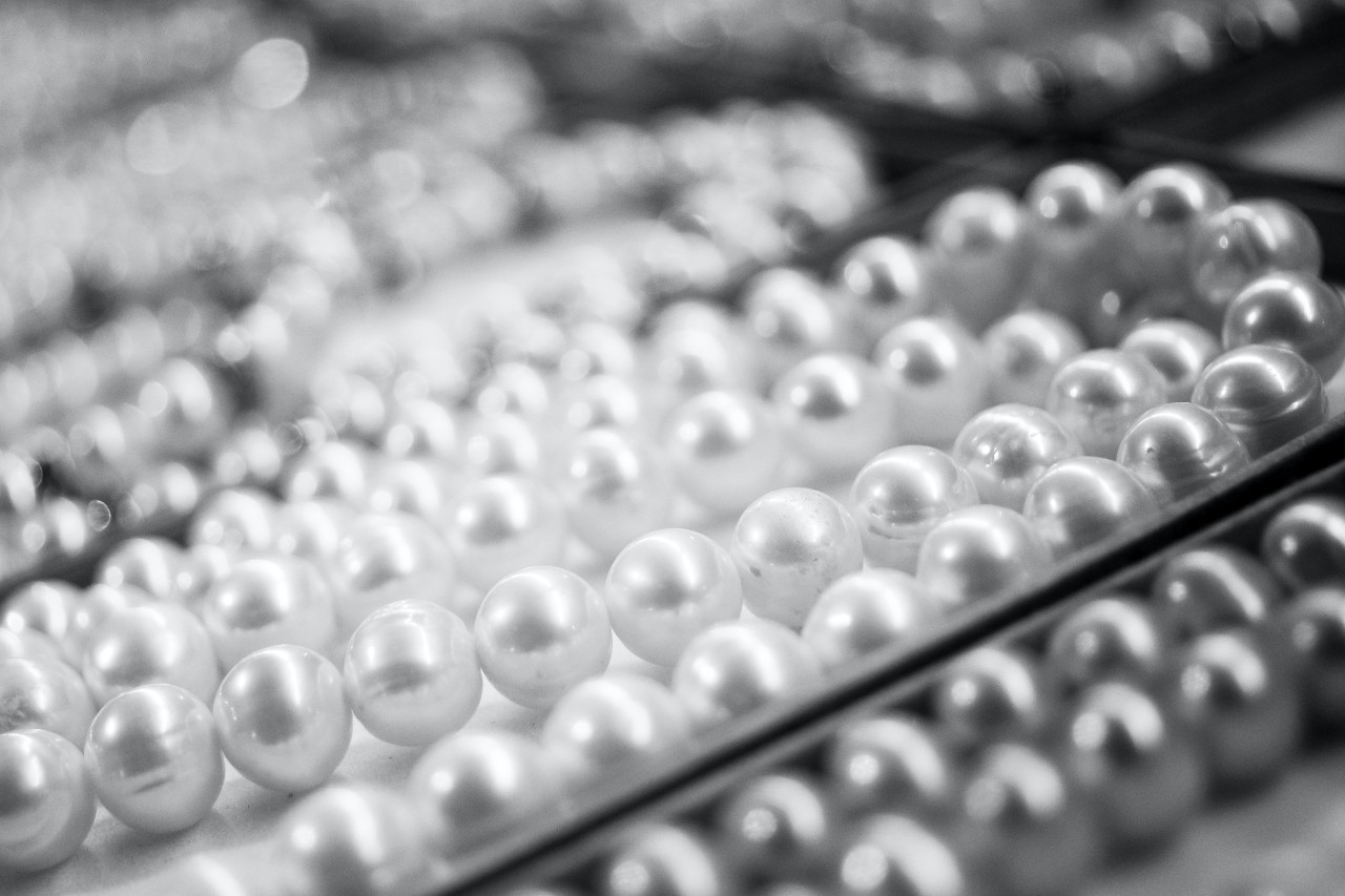 A black and white close-up image of several strings of pearls displayed in jewellery trays.