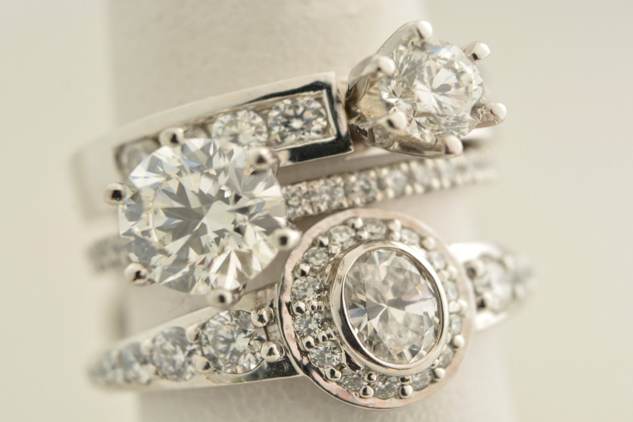 A stack of three white gold diamond rings with intricate designs on a soft background.