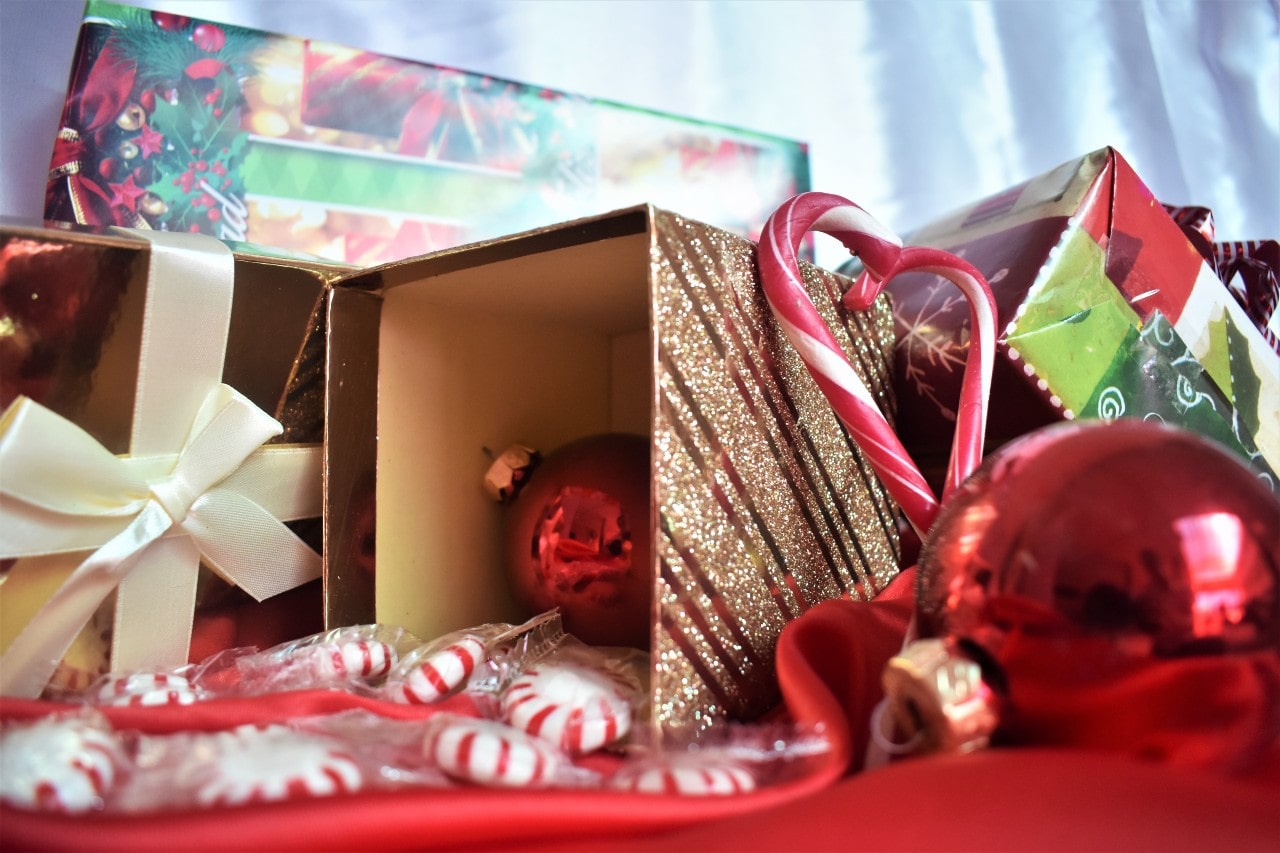 A festive arrangement of Christmas gifts, candy canes, red ornaments, and peppermint candies displayed with glittery and colourful wrapping.