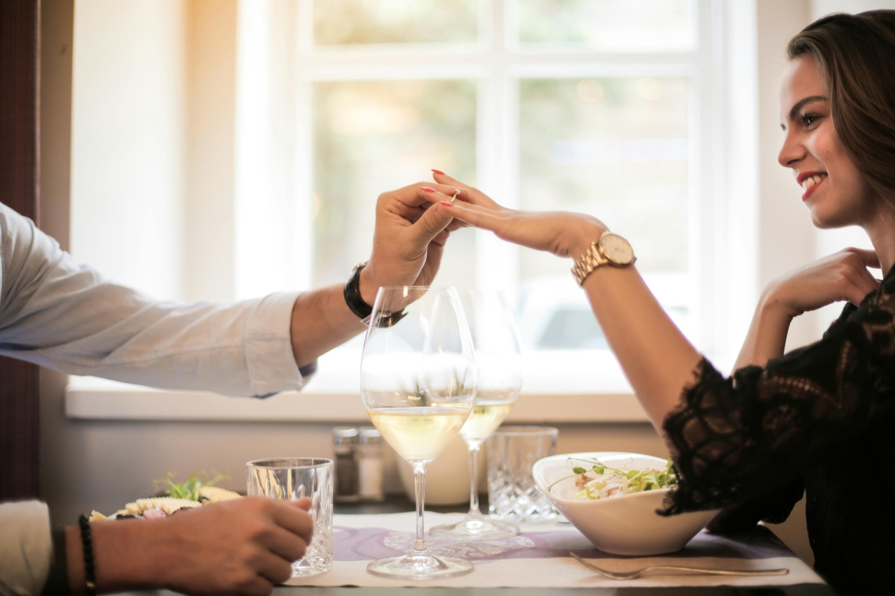 A close up of a couple dining in the restaurant, showcasing a man putting an engagement ring on a woman’s hand.