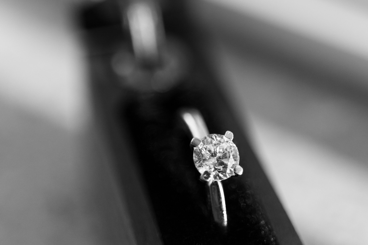 A close up of a silver solitaire round-cut diamond engagement ring against a blurry background of a black velvet box.