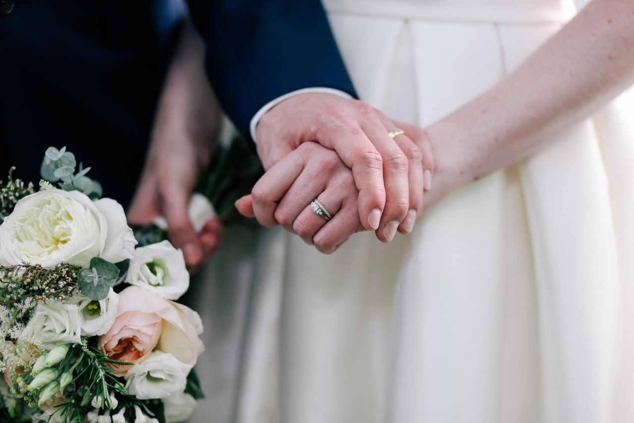 A close-up of a newlywed couple holding hands, showcasing their white gold wedding bands.