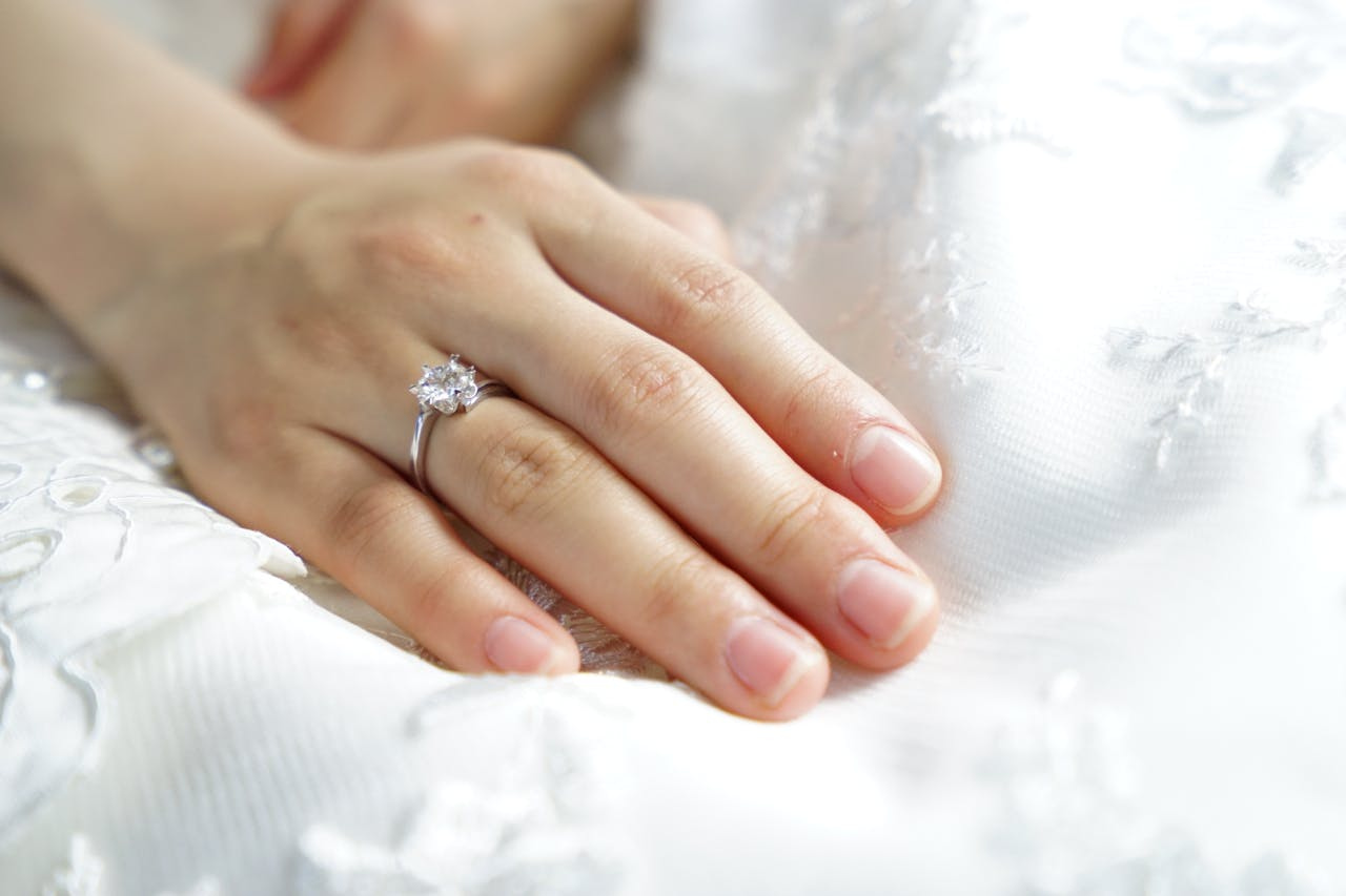 A close up of a bride&rsquo;s hand laying on top of white fabric, showcasing a white gold diamond engagement ring.