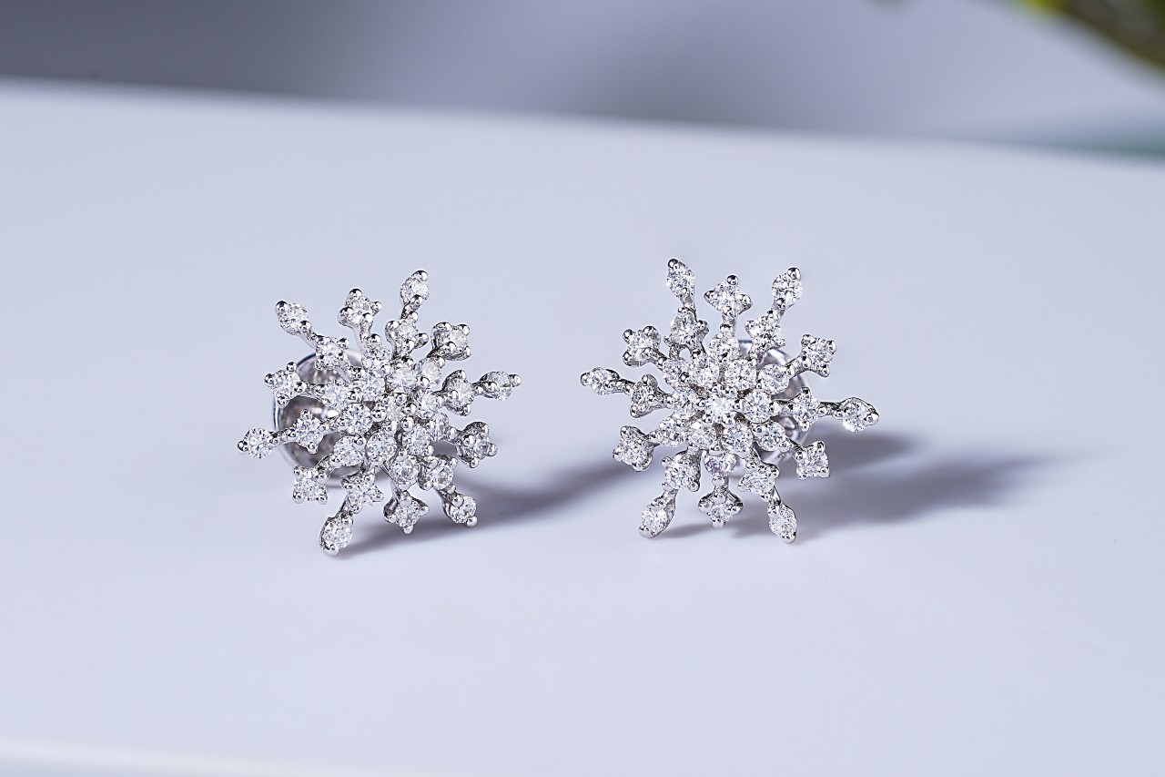 A pair of diamond earrings designed in the shape of snowflakes on a white background A pair of diamond earrings designed in the shape of snowflakes on a white background