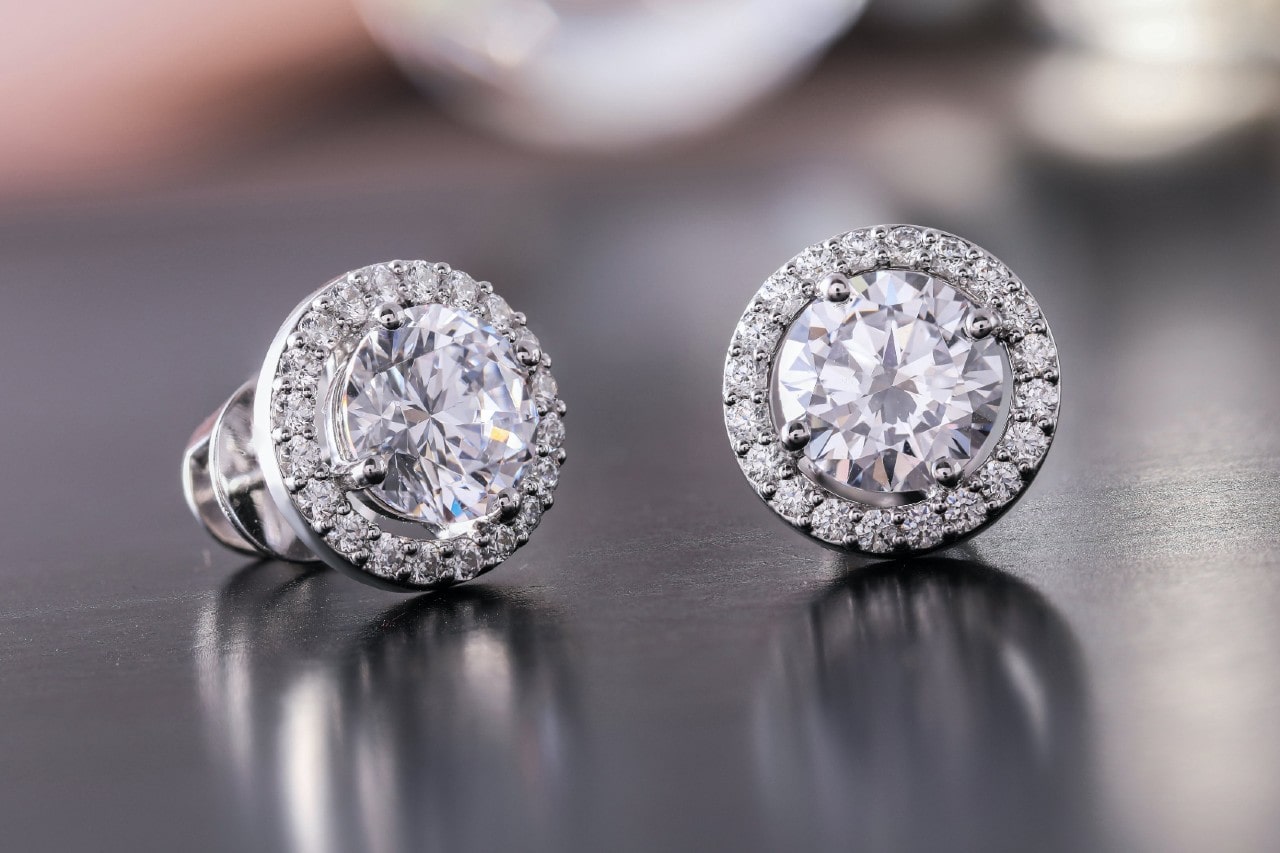 A pair of halo diamond earrings on a polished surface A pair of halo diamond earrings on a polished surface