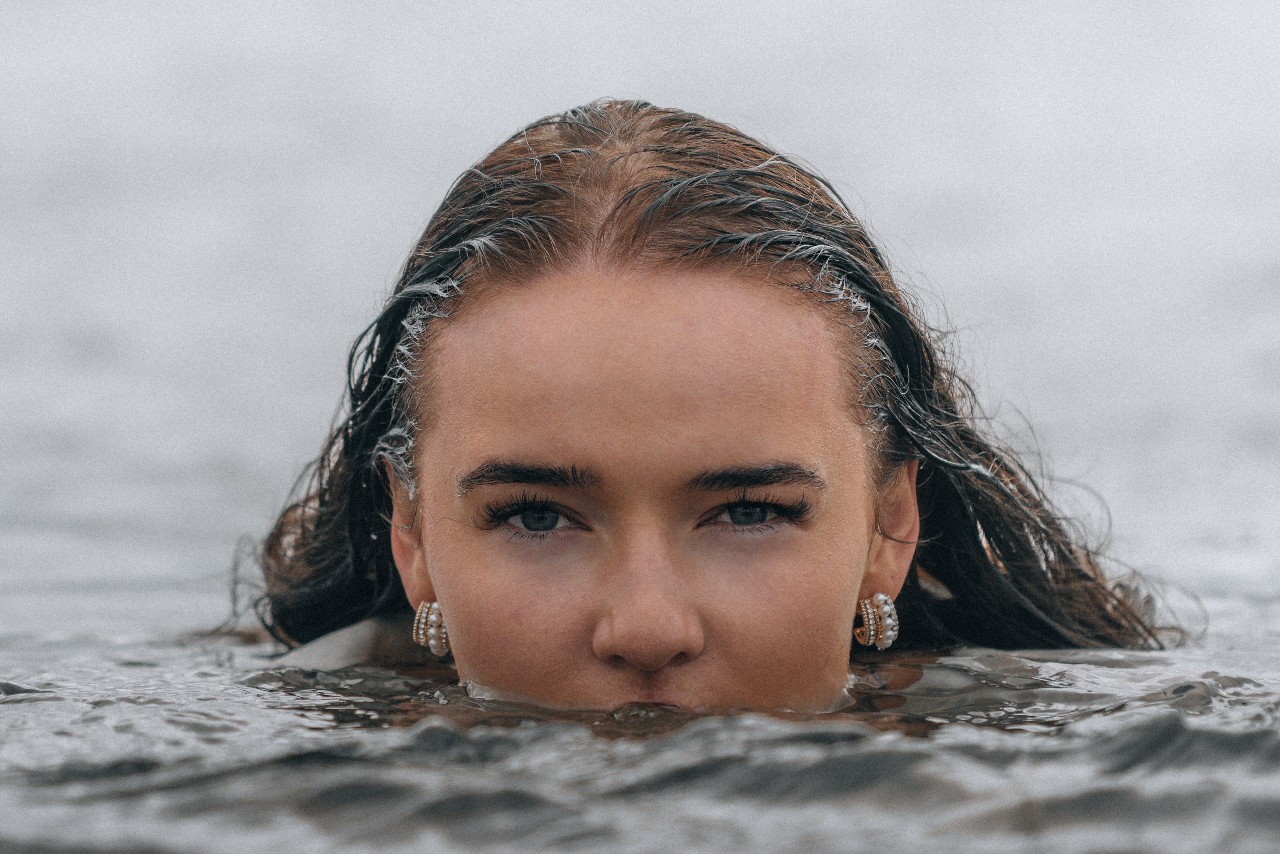 A woman whose face is half-submerged in water is wearing pearl huggies earrings