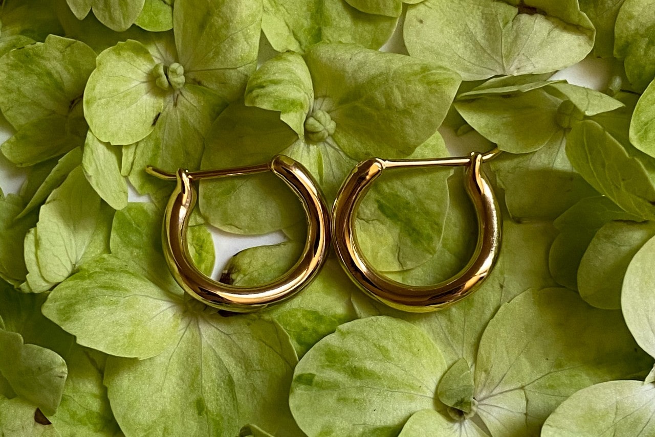 A pair of yellow gold huggies earrings on a bed of green leaves