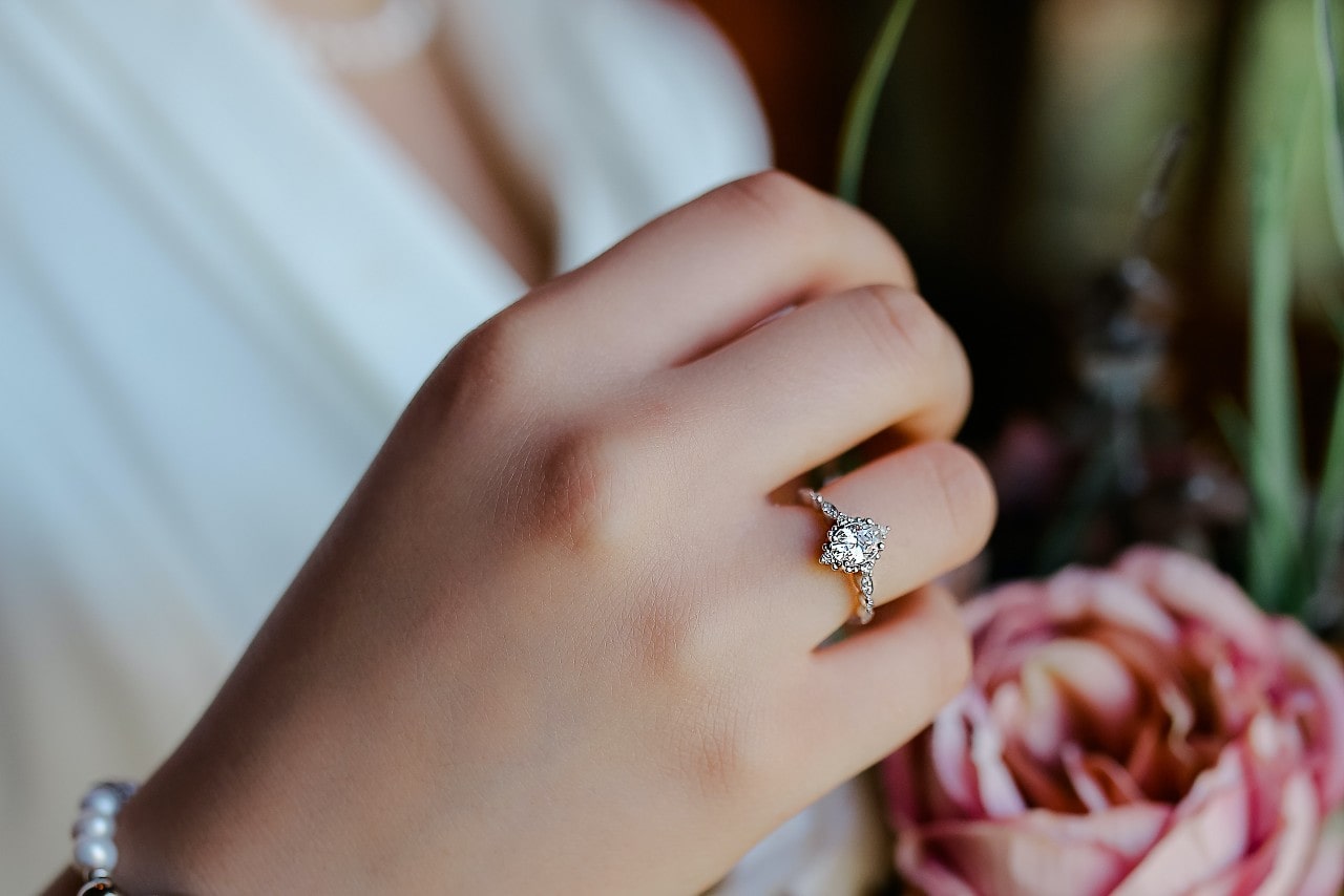 A close-up of a woman’s hand wearing a sparkling diamond engagement ring as she holds a pink rose in her other hand.