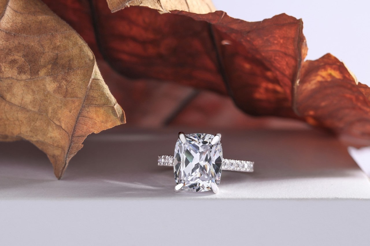 A white gold engagement ring with side stones under maple leaves