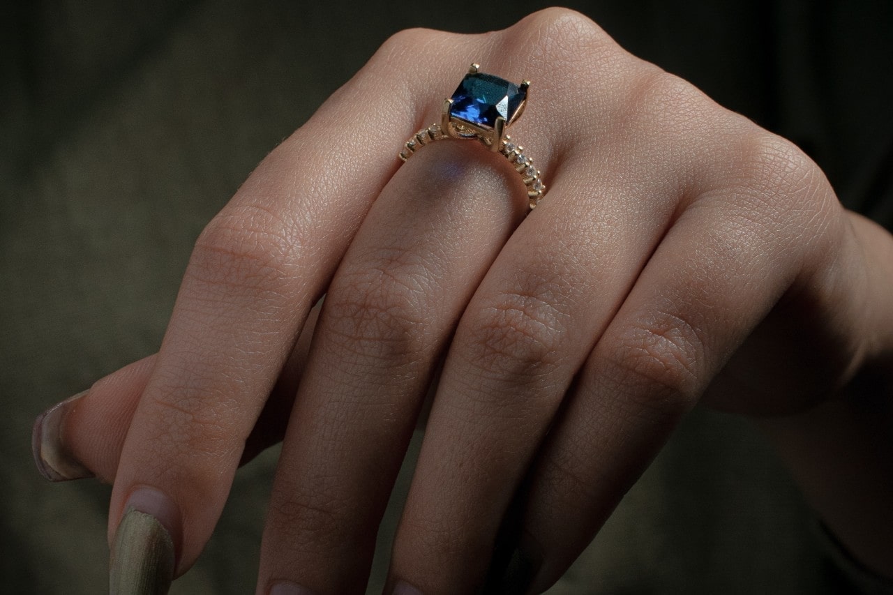 Lady's hand wearing a fashion ring with a blue gemstone and diamonds