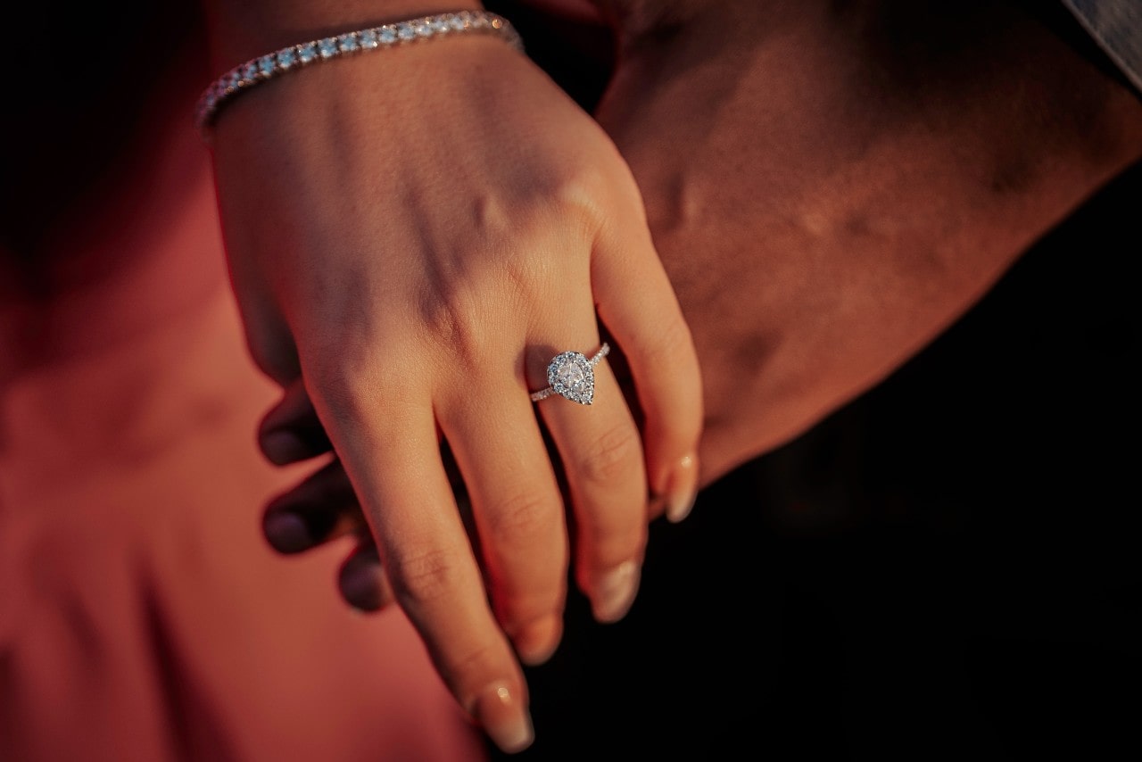 A close-up of a woman's hand adorned with a pear shaped white gold diamond halo engagement ring.