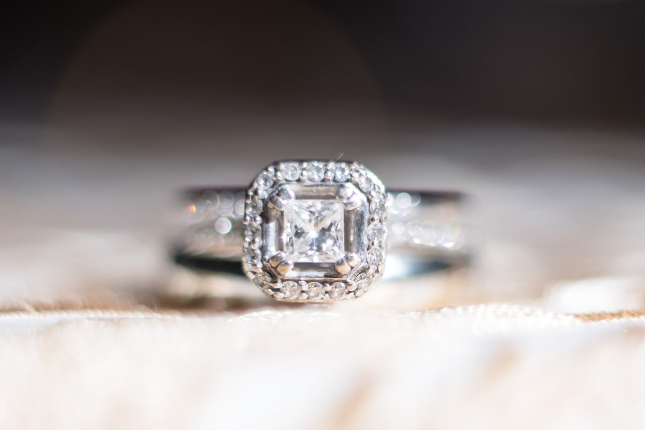 A white gold diamond halo engagement ring on top of a blurred surface.