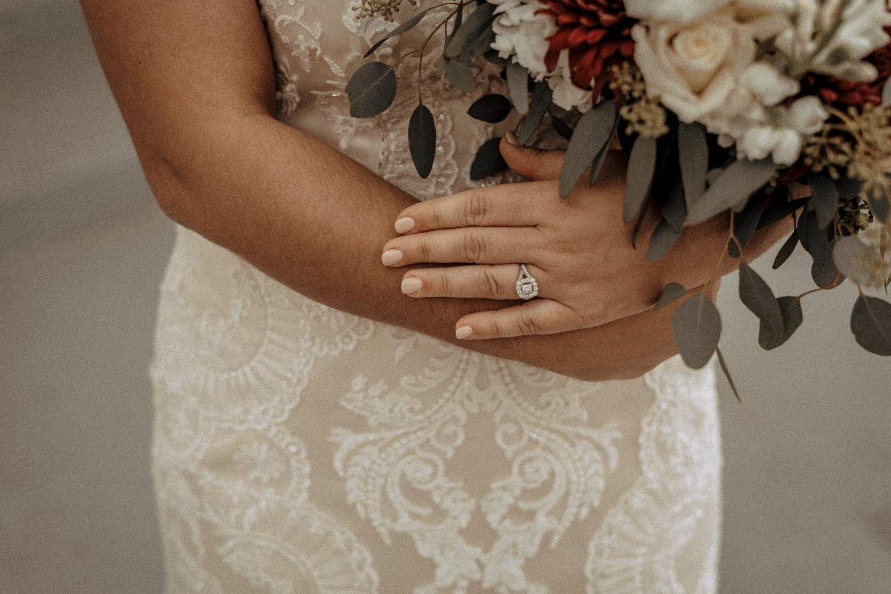 A bride holds her bouquet of flowers while wearing her princess-cut halo engagement ring