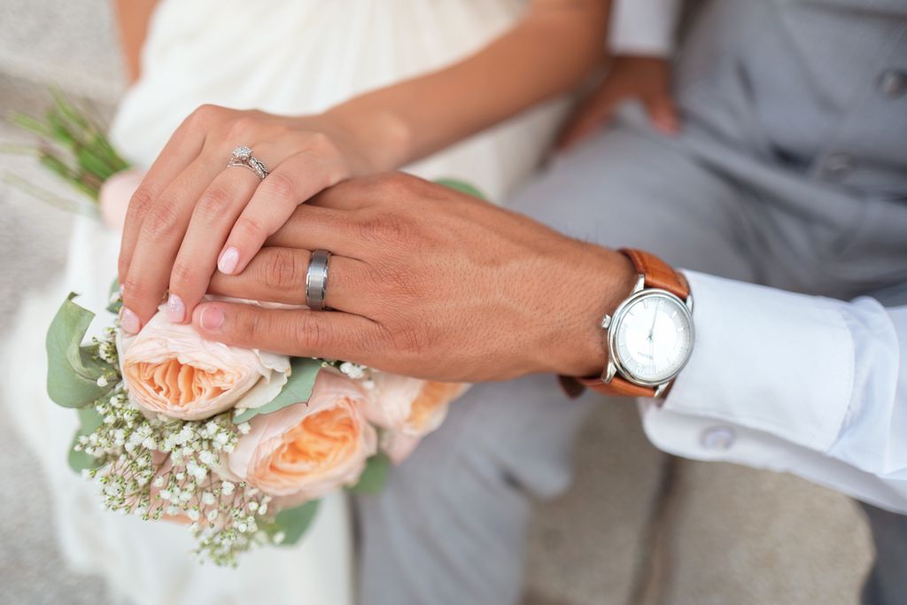 A bride and groom show their wedding rings while holding a bouquet of peach roses and white baby's breath flowers. A bride and groom show their wedding rings while holding a bouquet of peach roses and white baby's breath flowers.