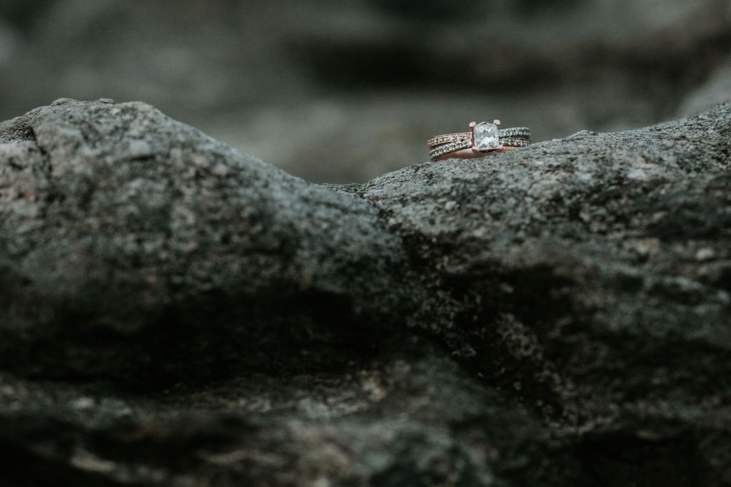 Princess cut ring with mixed metal band sitting on a rock