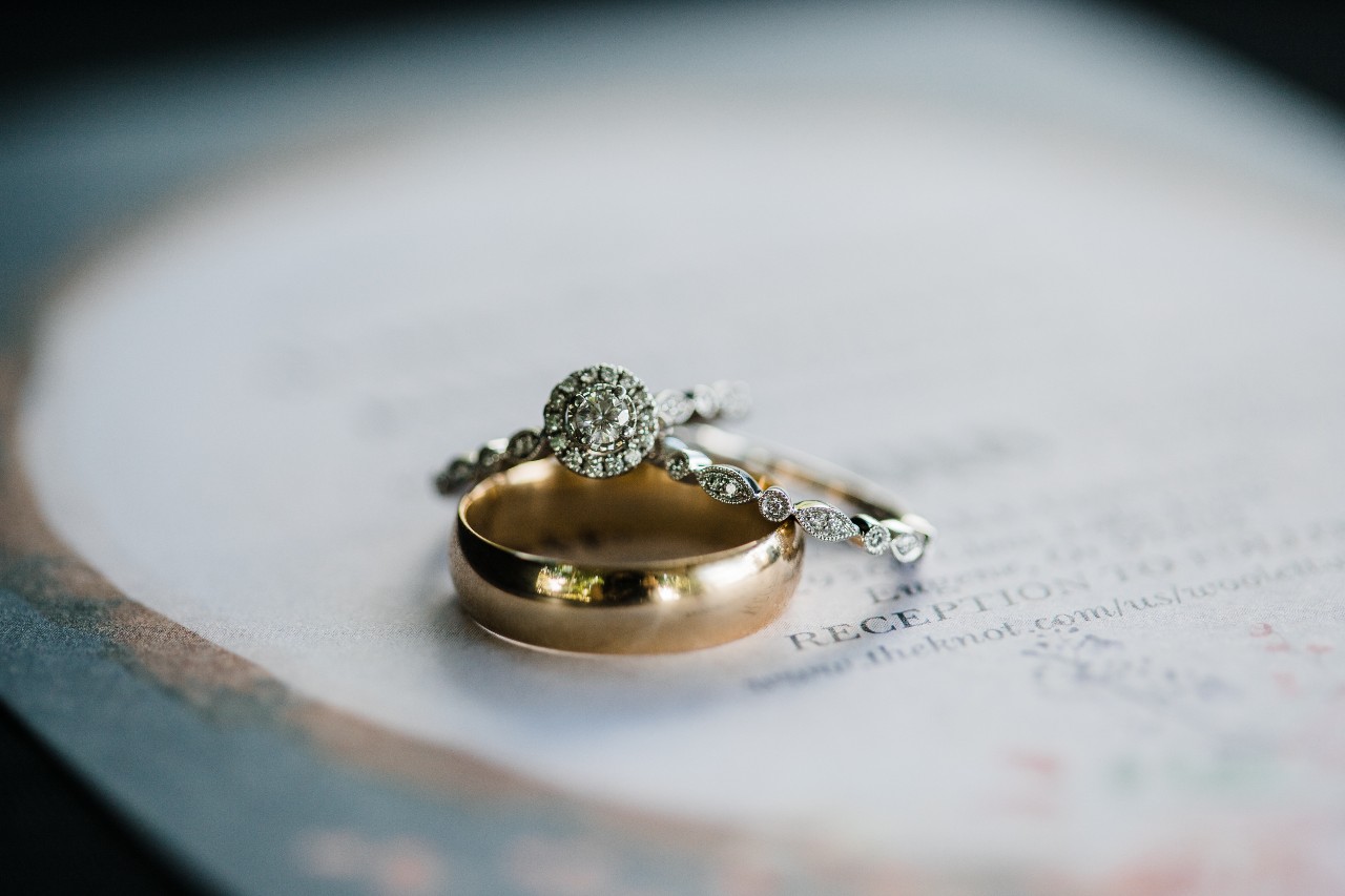 A vintage halo engagement ring with a matching band and gold band sitting on a wedding invitation