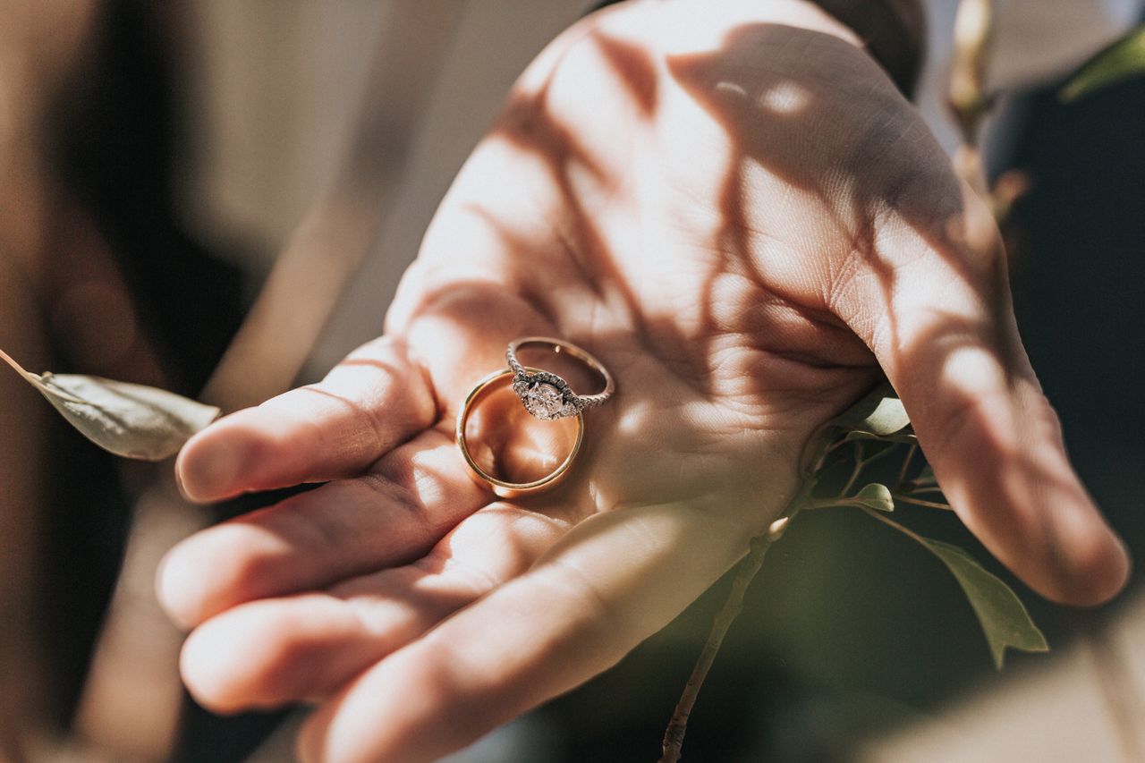A three-stone round cut ring sits with a gold band in a palm of a hand