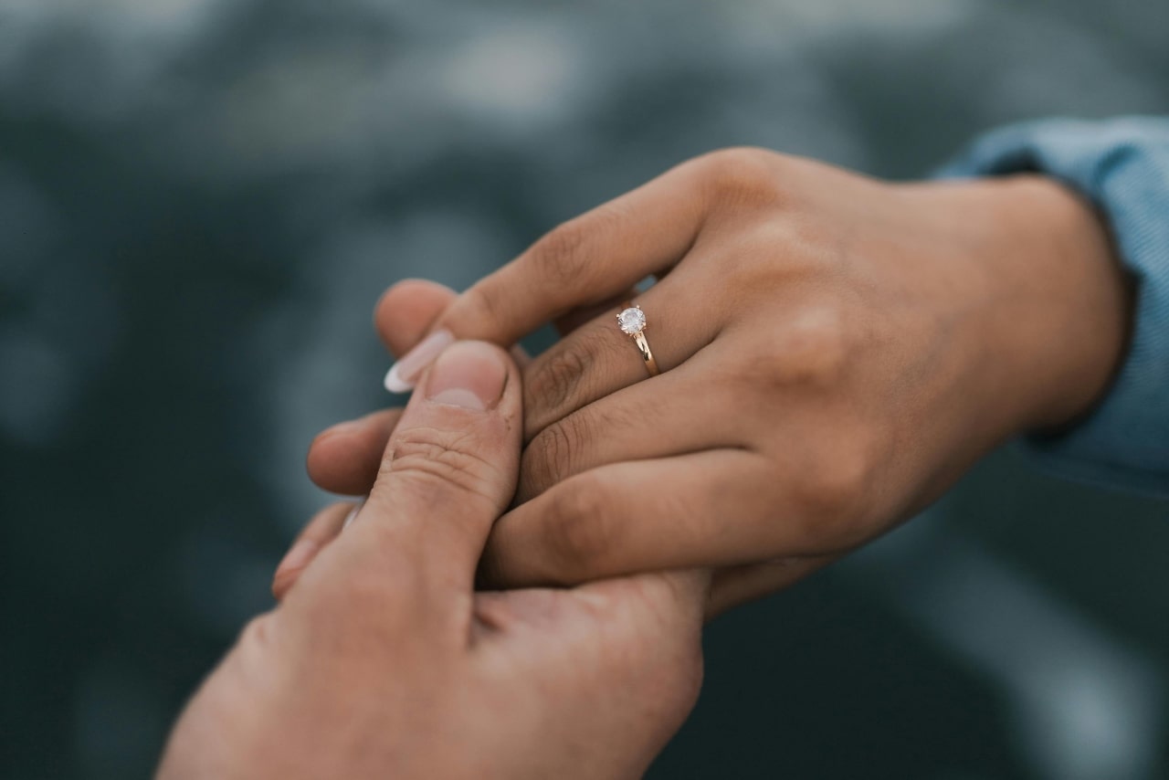 A close up of two hands, showcasing a yellow gold solitaire diamond engagement ring