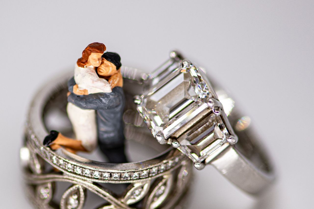 A wedding cake topper sits with a wedding band and engagement ring from TACORI