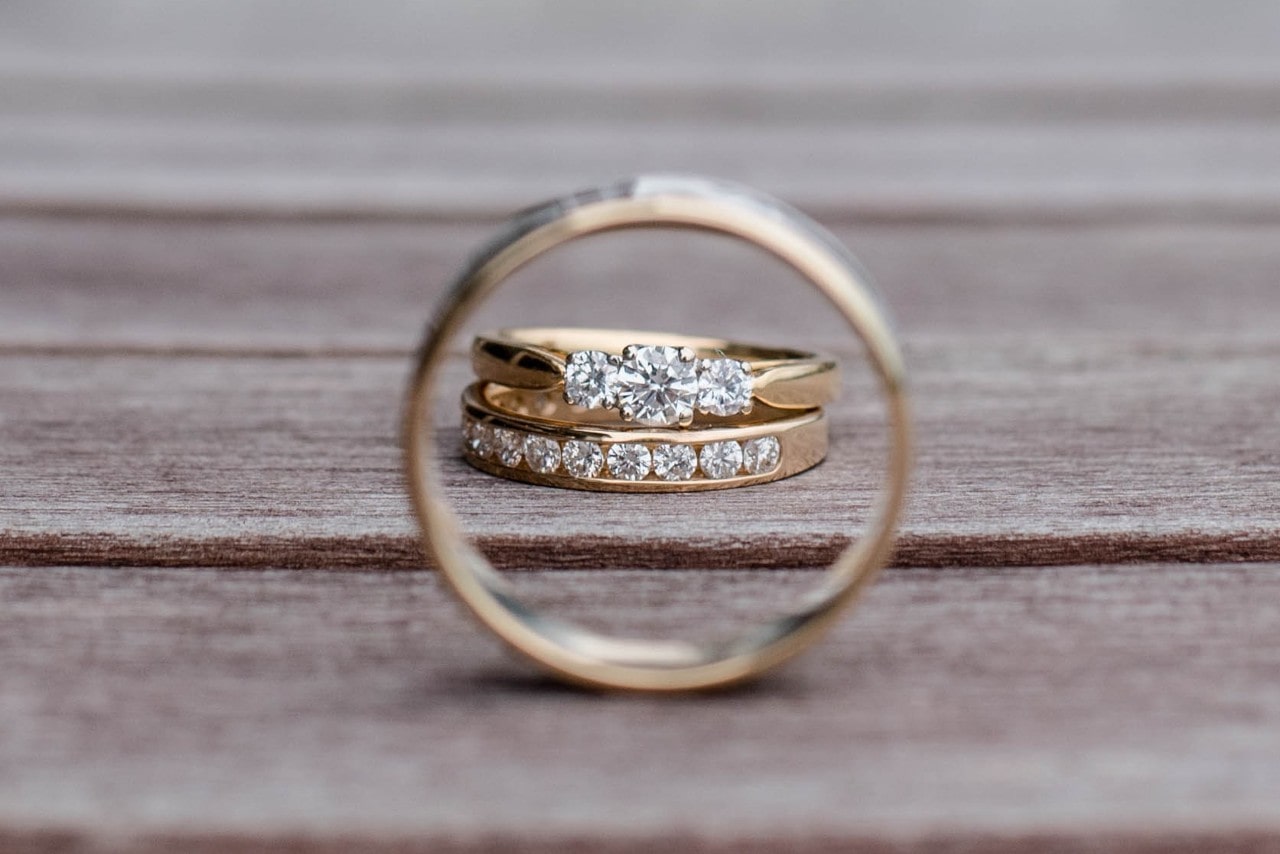 A close-up of two gold diamond rings perfectly aligned through the circle of a third gold band on a wooden surface.