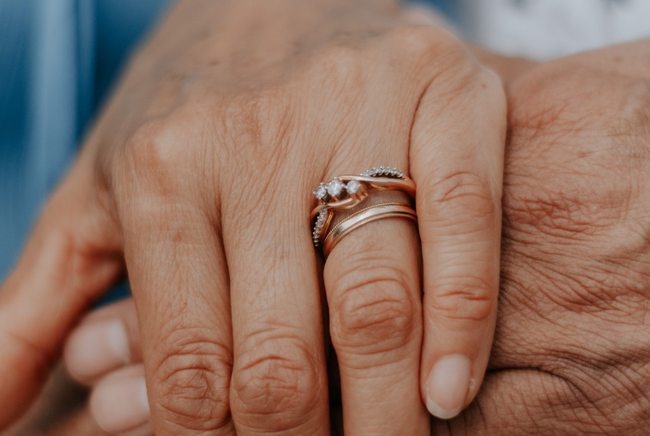 Close-up of two hands gently holding, with one wearing a rose gold engagement ring and wedding band featuring small diamonds in an intertwined design.