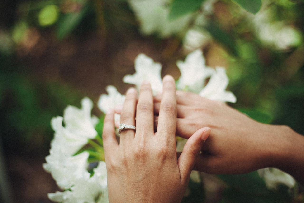 An engaged couple lays their hands on a bouquet of flowers.