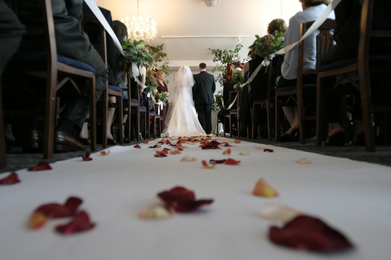 A bride walks with her father down a rose petal-covered aisle in a church venue