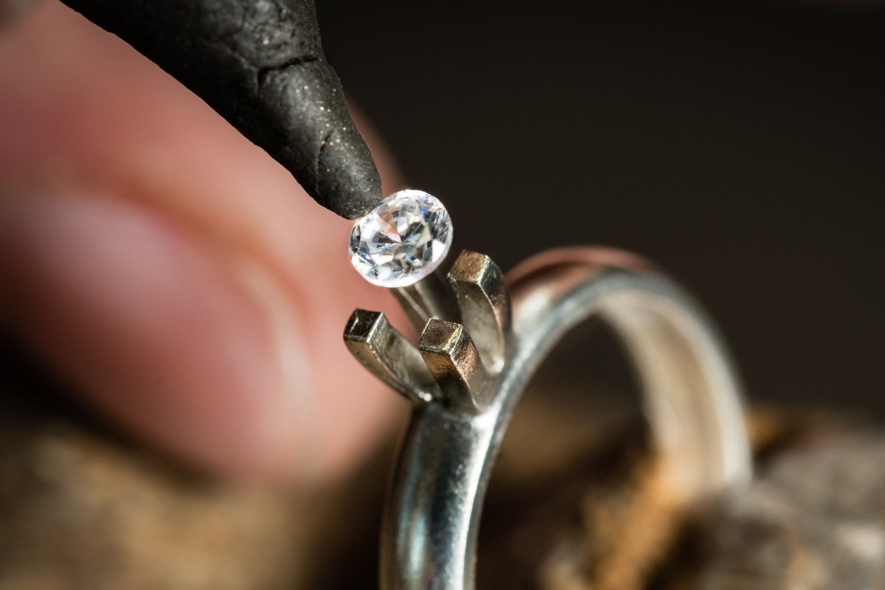 A professional gemologist carefully places a lab-grown round-cut diamond into the prongs of a platinum solitaire engagement ring