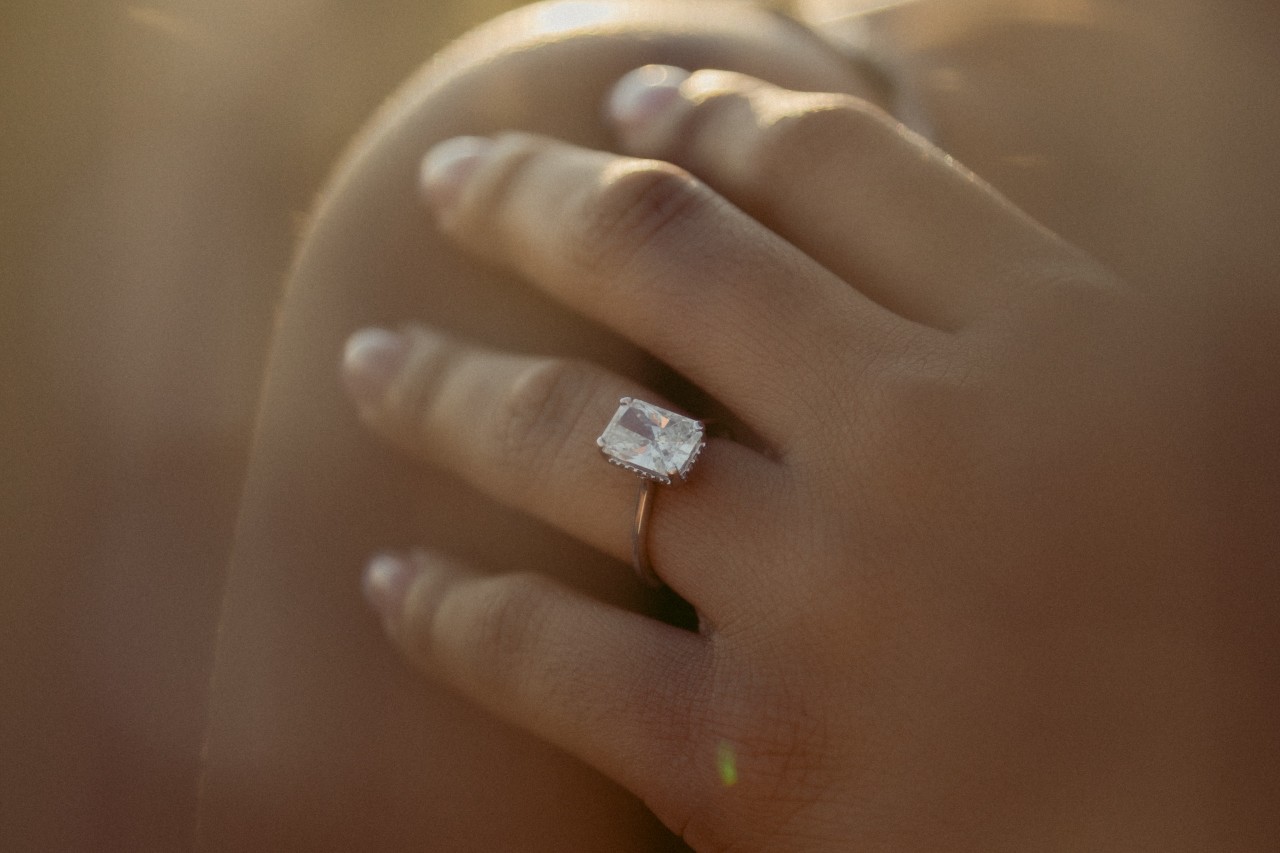 lady’s hand wearing an emerald cut solitaire engagement ring