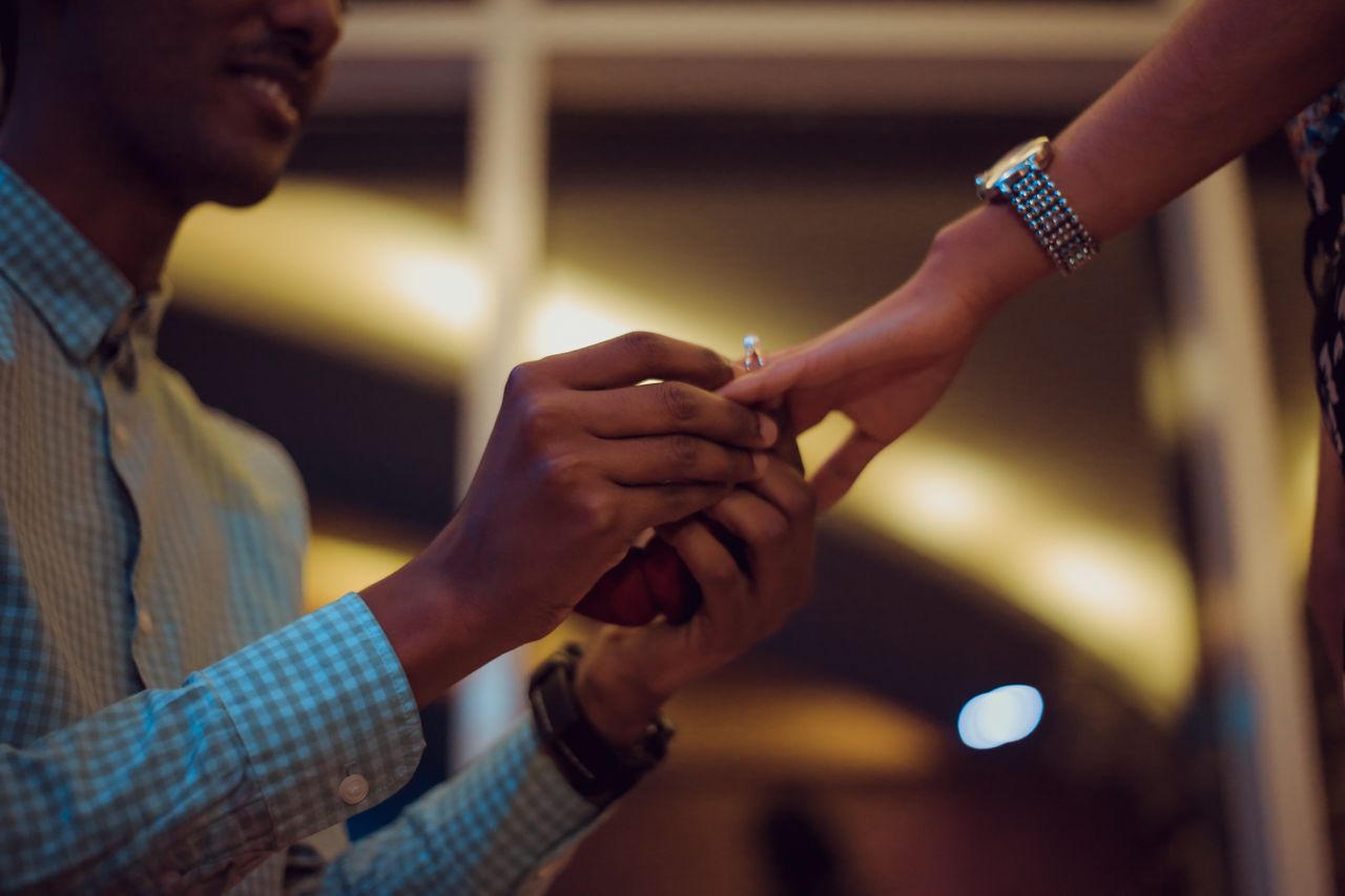 A man on one knee slips an engagement ring on a woman’s hand during the evening.