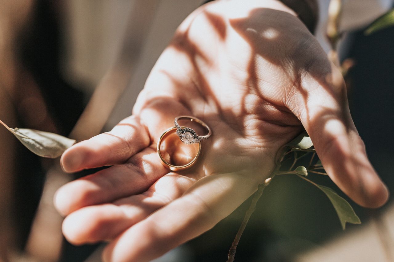 A three stone round-cut ring sits with a gold band in a palm of a hand.