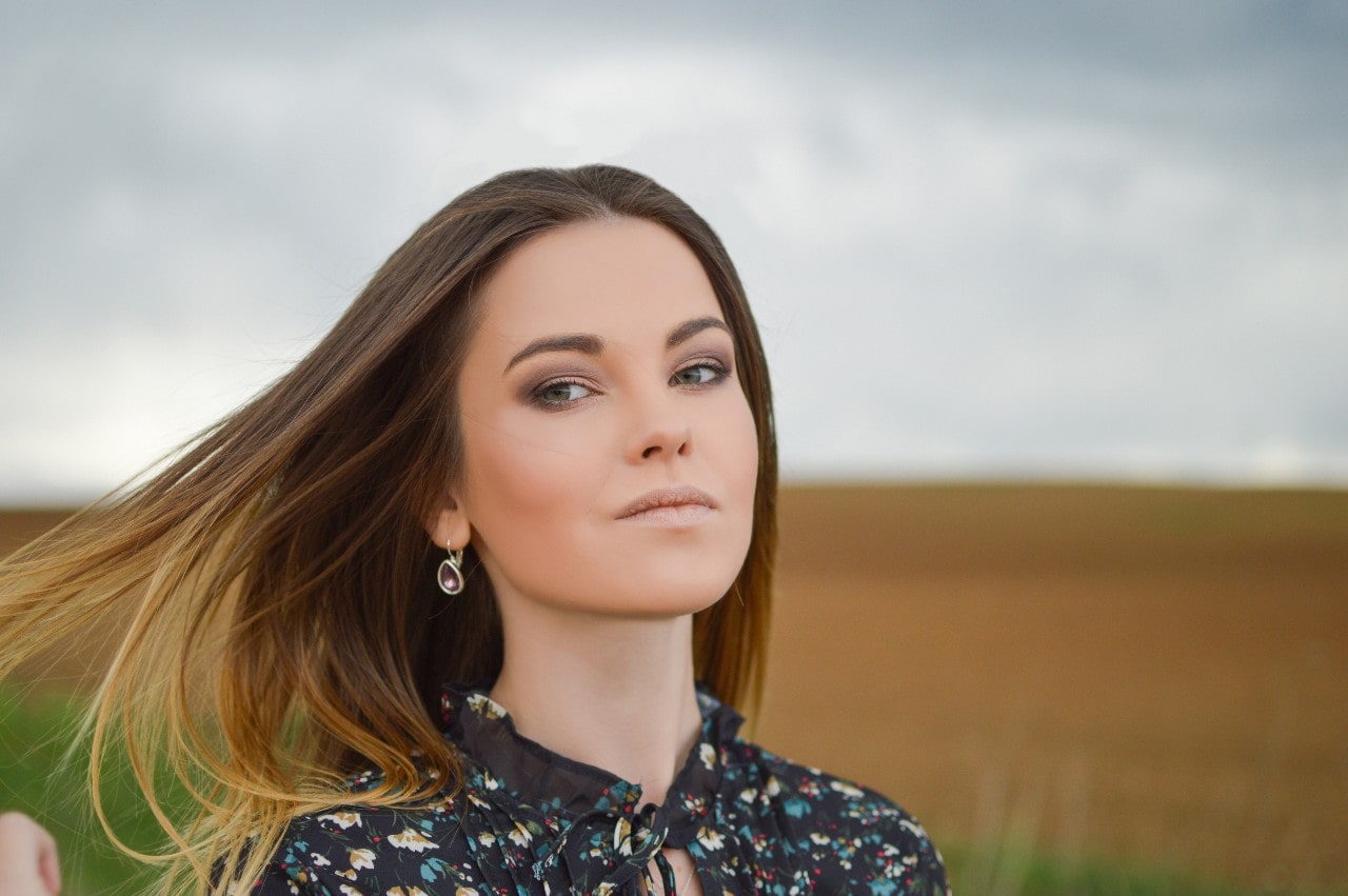 A woman in a floral blouse wears TACORI gemstone drop earrings by a field