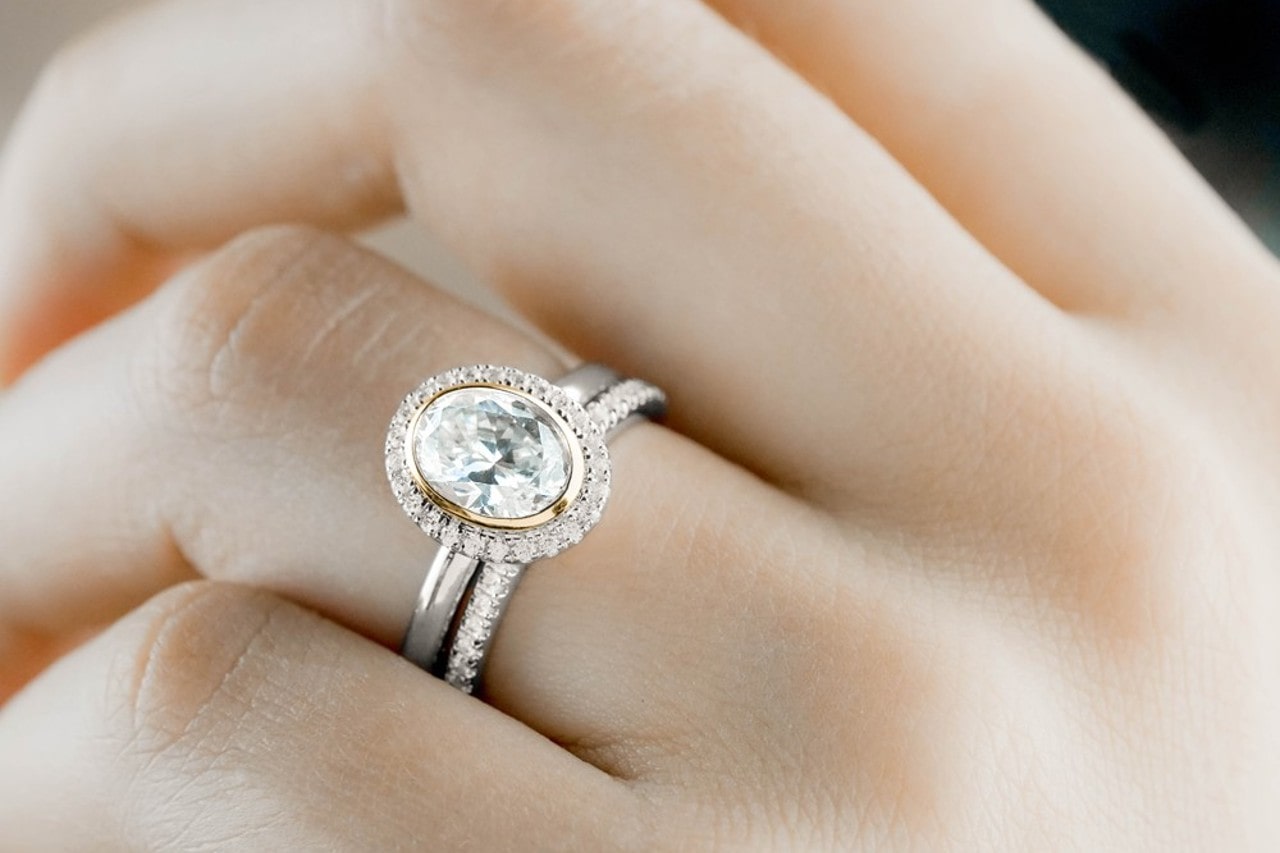 Close up image of a hand wearing a silver and gold engagement ring and diamond wedding band