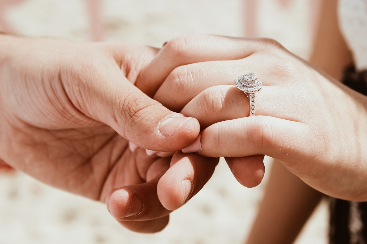 a man holds a woman’s hand to inspect her halo engagement ring.