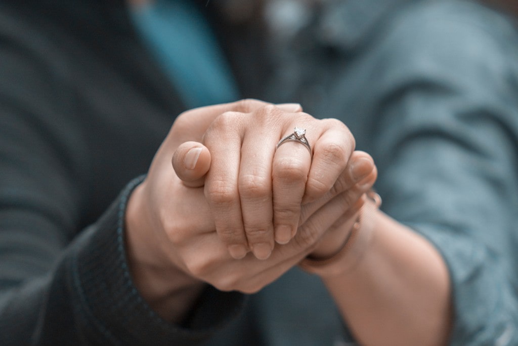 An engaged couple holds hands, showing off an engagement ring.