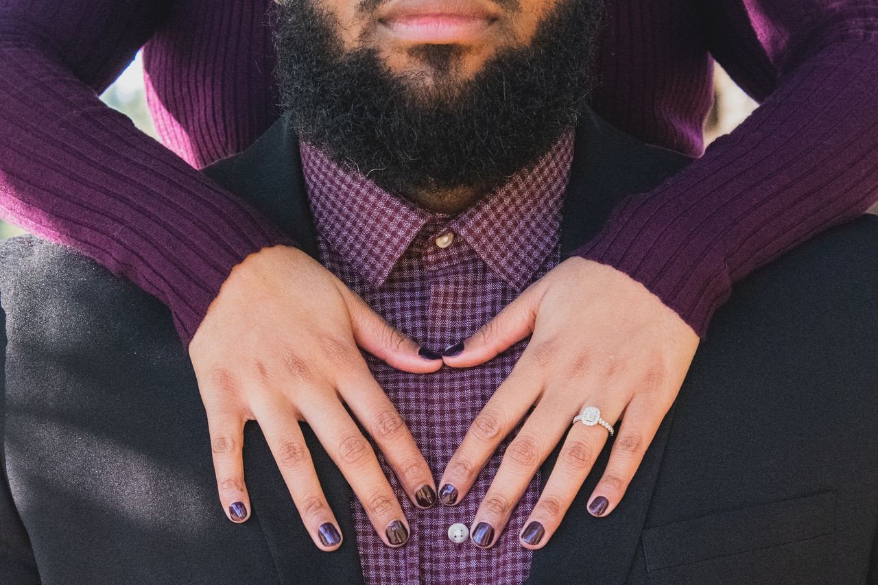 A woman places her hands on a man’s chest, showing off her halo engagement ring.