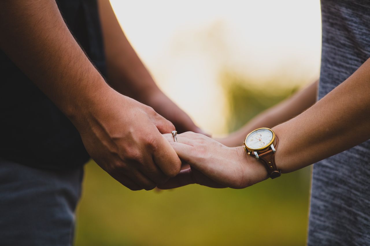 A woman and man holding hands, while the woman wears a solitaire engagement ring