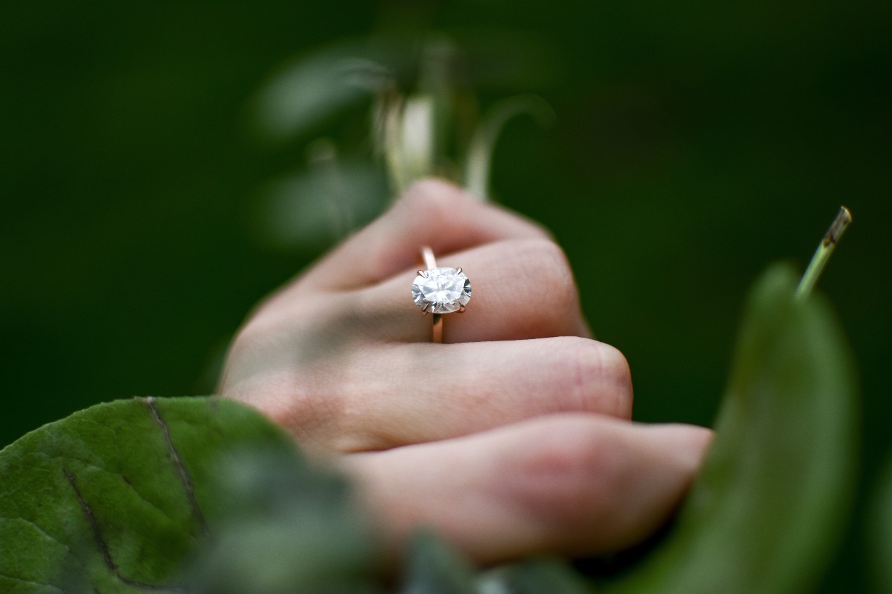 an oval cut diamond solitaire engagement ring on a woman’s finger as she grabs a plant.