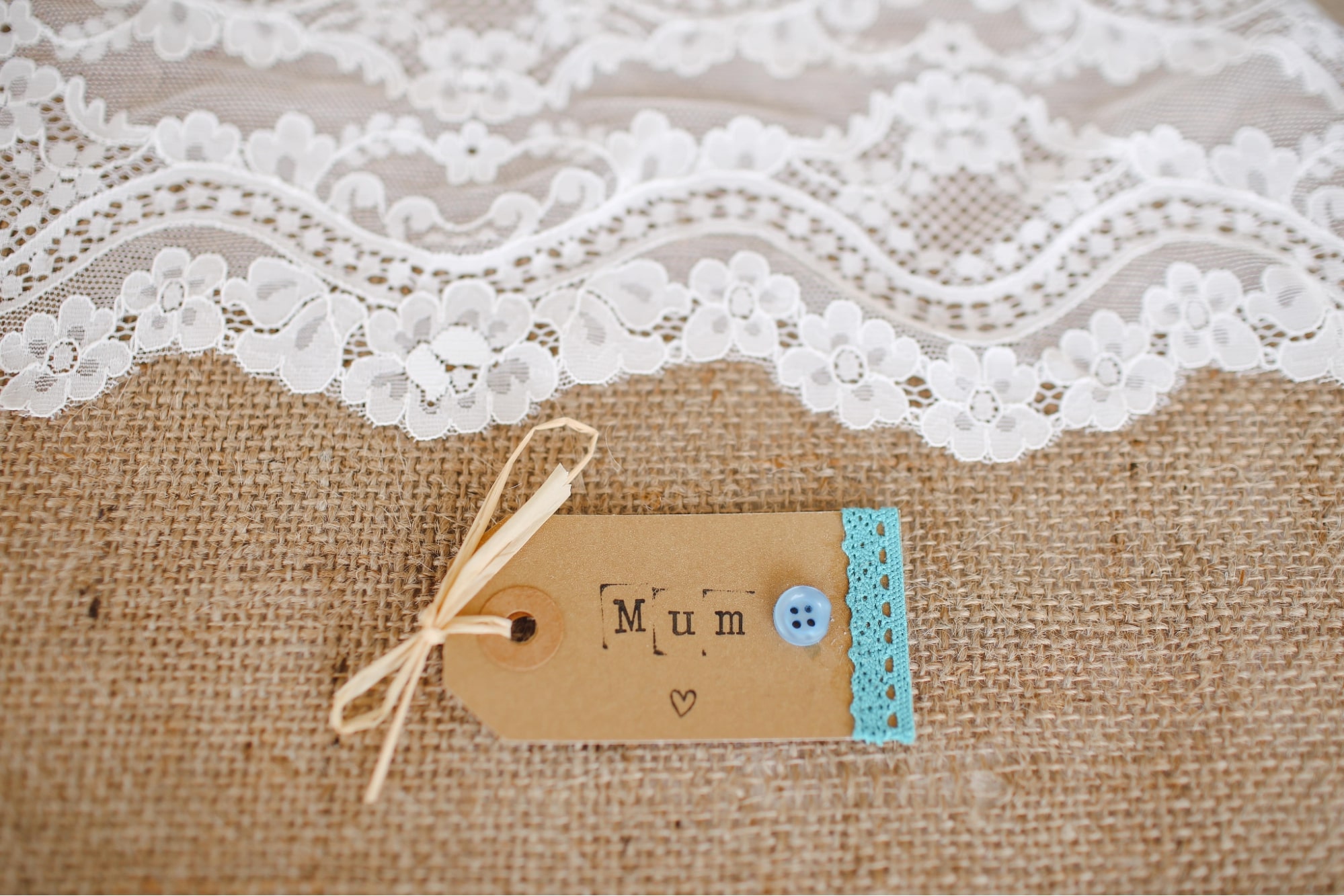 A handmade tag for a Mother’s Day gift on a burlap and lace table runner