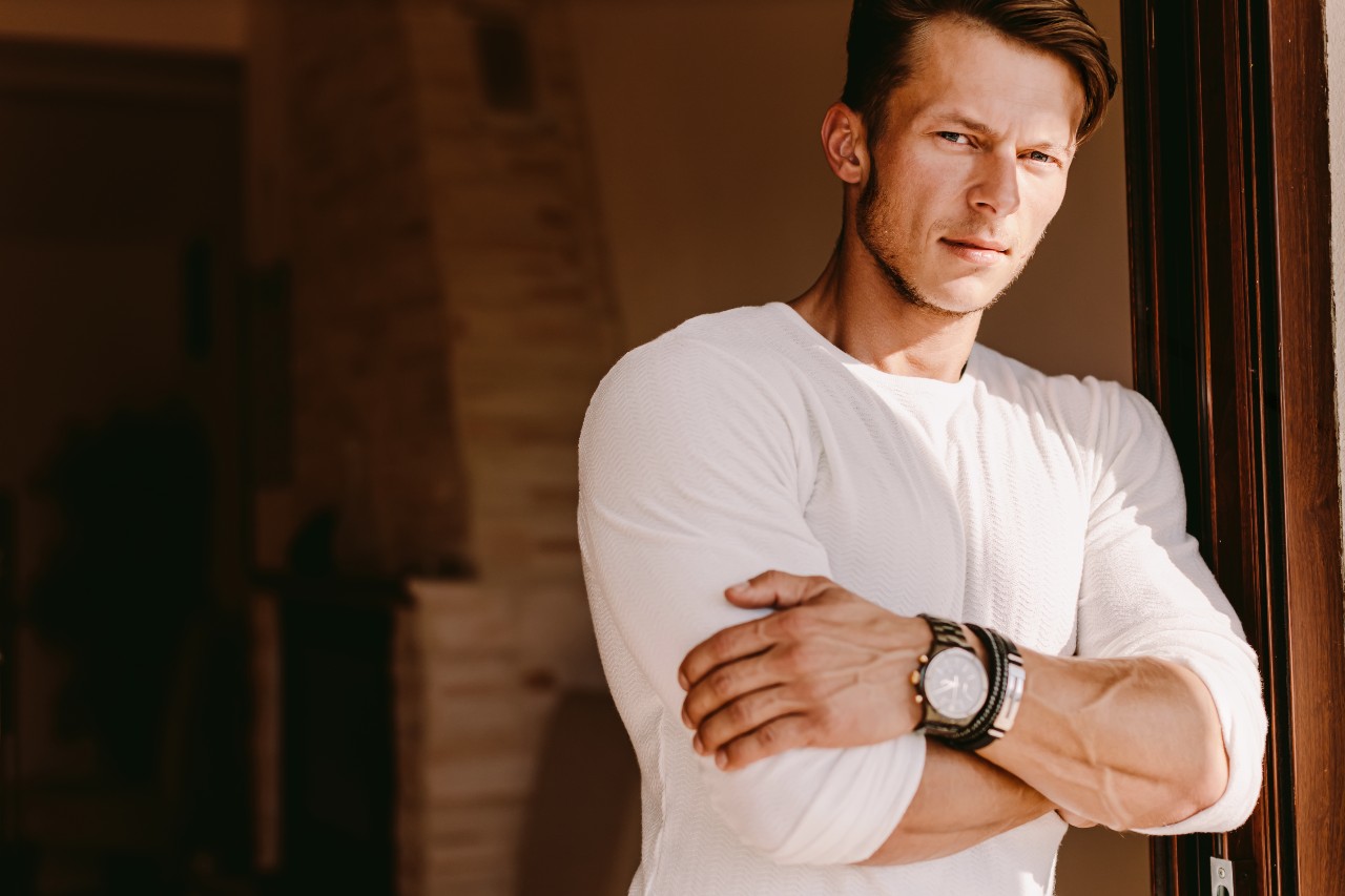 A young dad leans against the door frame on a Saturday morning while sporting a watch and bracelets