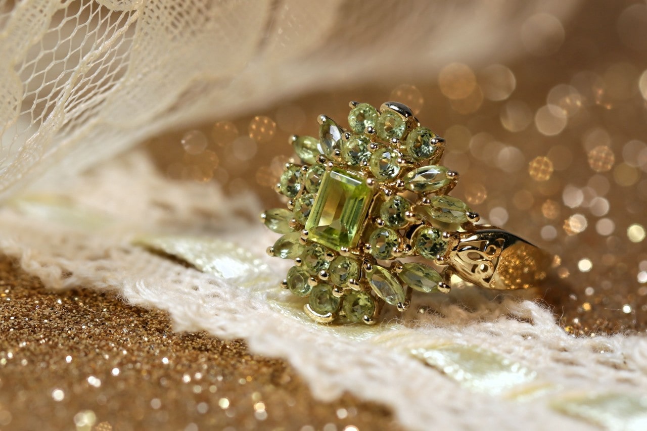 An elaborate peridot halo fashion ring on a gold glittery surface