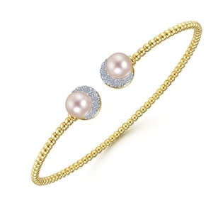 A yellow gold cuff features two pink pearls and diamond accents
