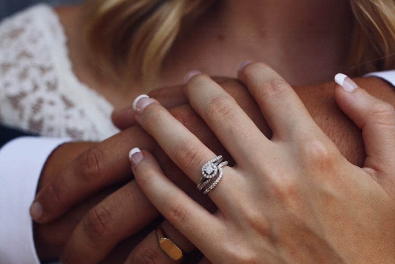 A woman’s hand wearing an engagement ring clasping a man’s hand