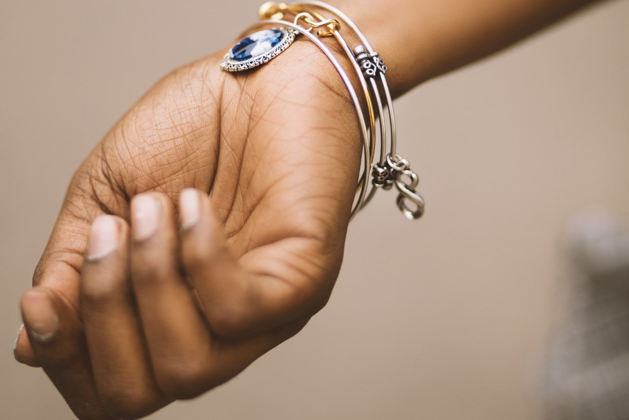 A woman wearing charm bracelets shows off a sapphire charm.