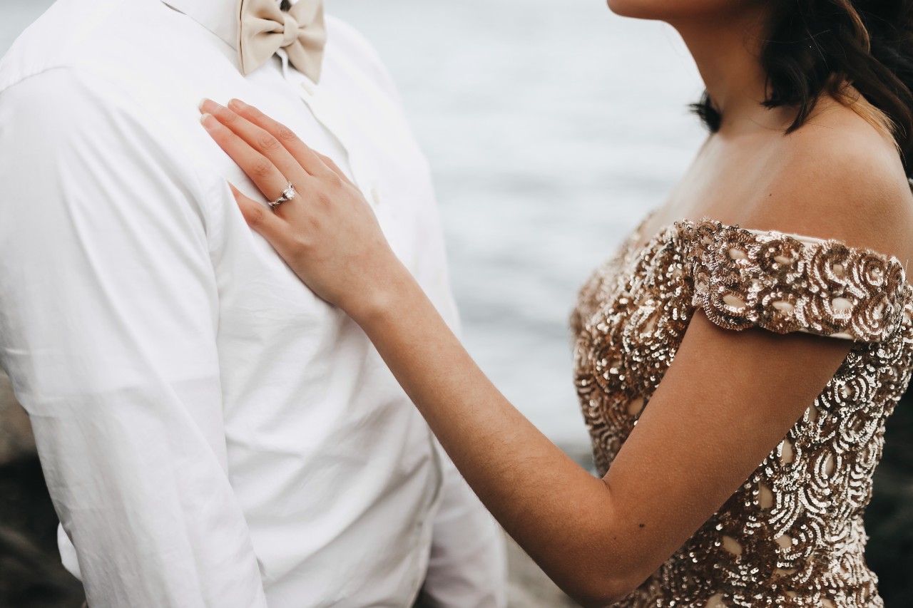 A couple wearing formal clothes embraces by a river.