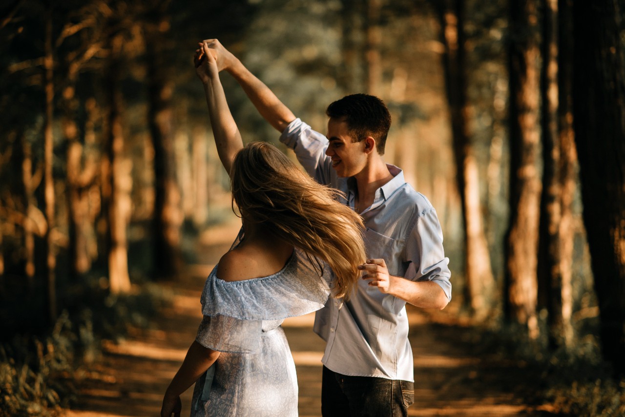 A couple dances while hiking through a fall trail.