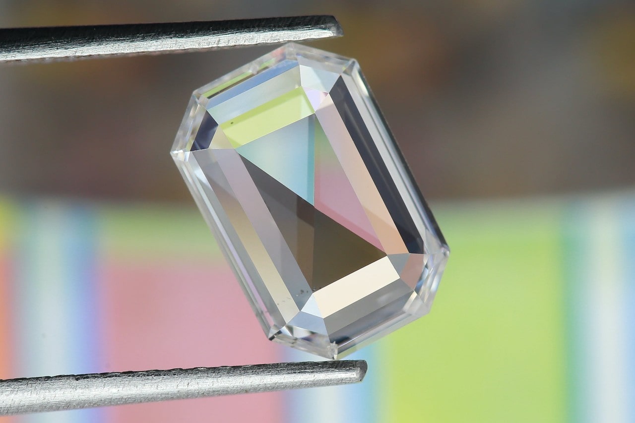 an emerald cut diamond being held close to the camera between tweezers